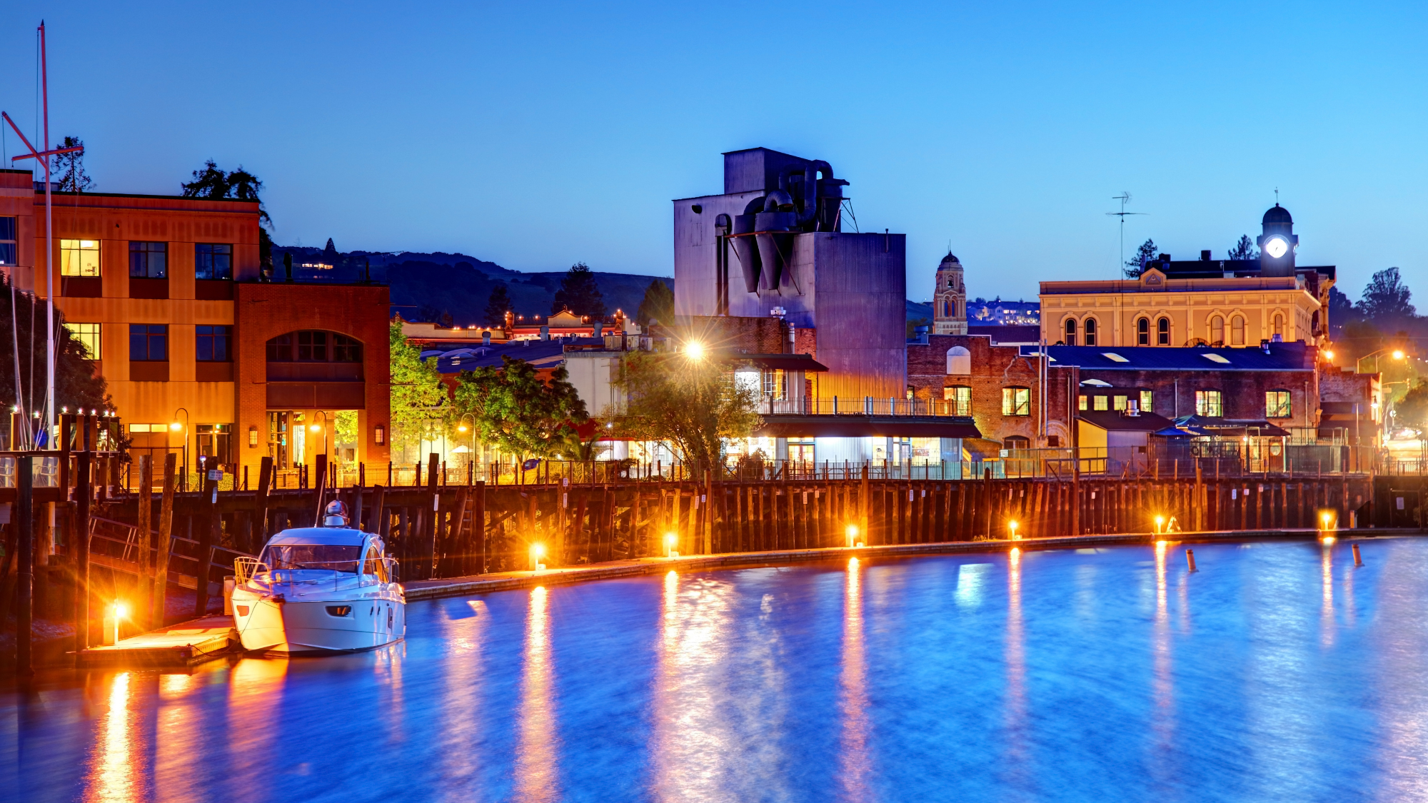 Petaluma waterfront at dusk with illuminated buildings and a docked boat